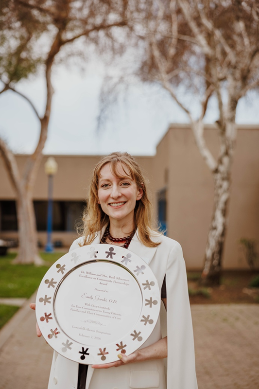A woman in white jacket stands outdoors holding a round silver platter.