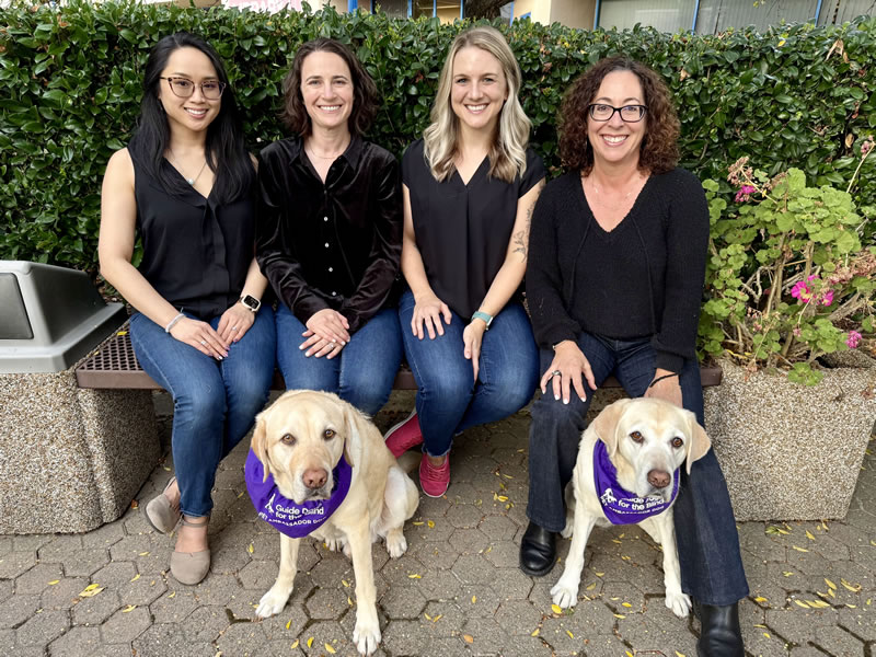 The four assessment center members: May Nguyen is on the outter left, Shelby Zimmerman and Rebecka Henry are in the middle, and to the far right is Stephanie Herlich. There are 2 light brown dogs wearing purple ties.
