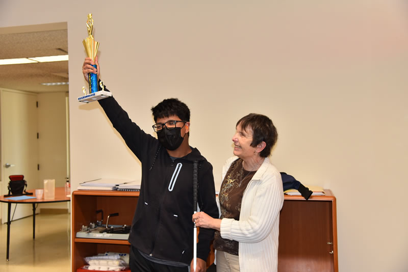 A student holding up a trophy posing next to a teacher. 