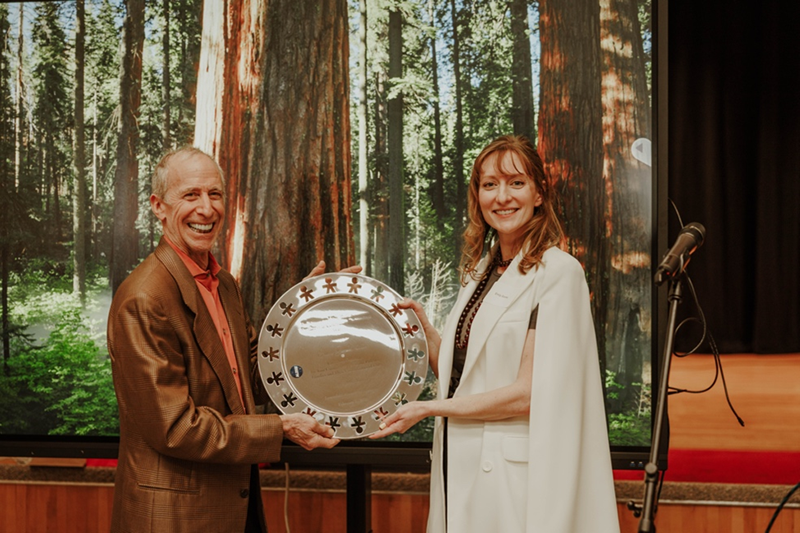 A man and a woman holding a silver platter award pose for a photo.
