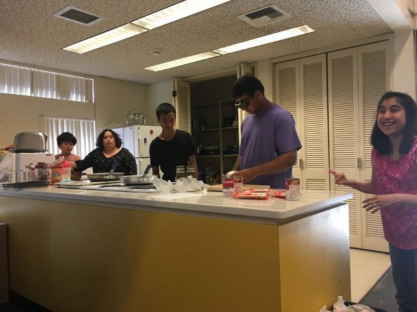 Five students preparing food together around a kitchen island.