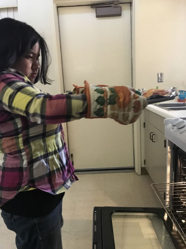 A student removes a tray of food for dinner from the oven.