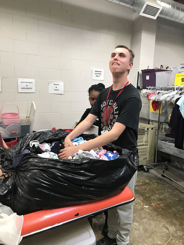 A student from the applied academics program is sorting clothes from a bag. He has a huge smile on his face as he performs this task!