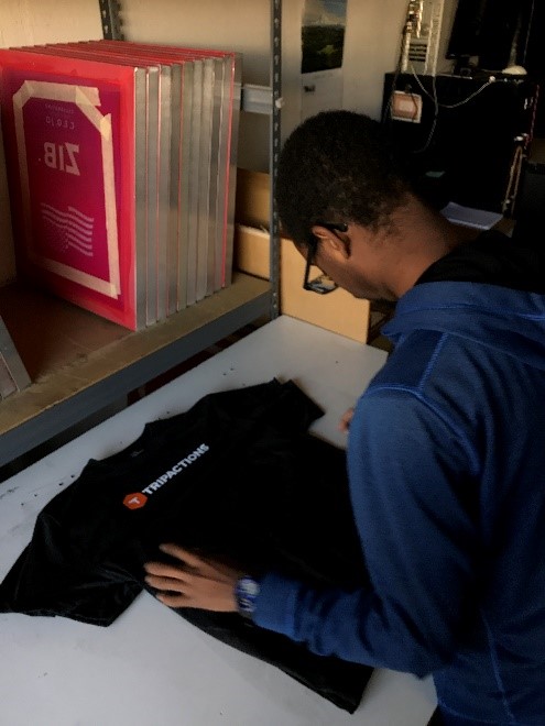 A student working at a T-Shirt printing shop is folding a shirt.