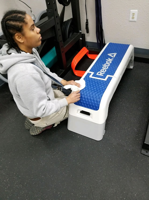 A student in the Life Skills program is wiping down cardio equipment at a local job site.