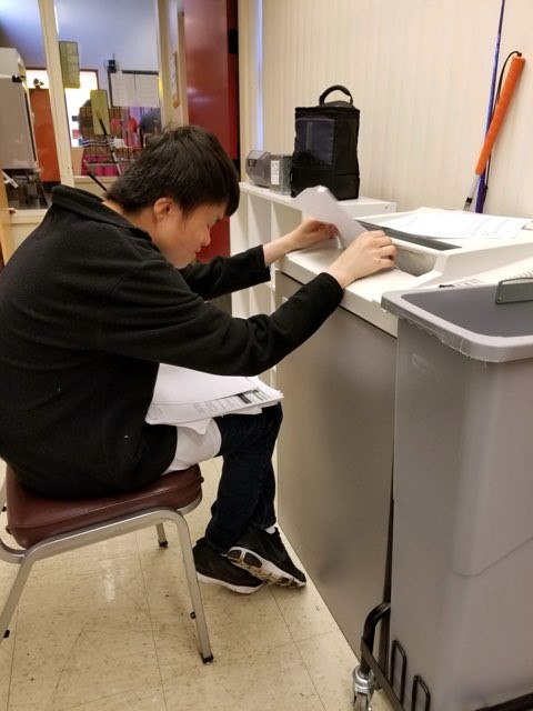 A student feeding paper into a paper shredder at an on campus thrift store, The Closet.