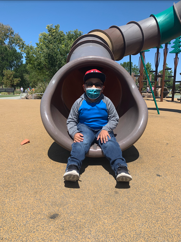 A student sits at the bottom of a big gray and green slide to pose for a picture.