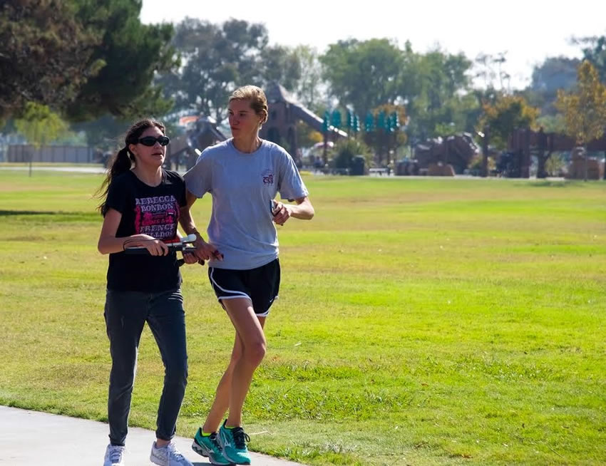 A teacher uses a tether to guide a student during a run at a nearby park.