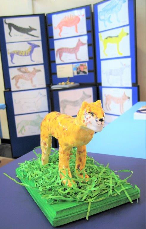 Ceramic cheetah standing on shredded green paper grass on a green wooden base.