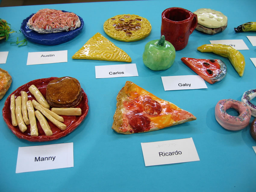 Ceramic cup, pizza, spaghetti, burger and fries, apple, donuts, and other snacks.