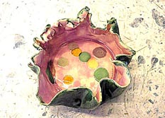 Round ceramic bowl, with ruffle top, green exterior, and pink interior.
