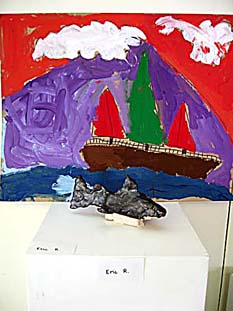 Shark sculpture in foreground, and painting of a ship in the ocean in the background.