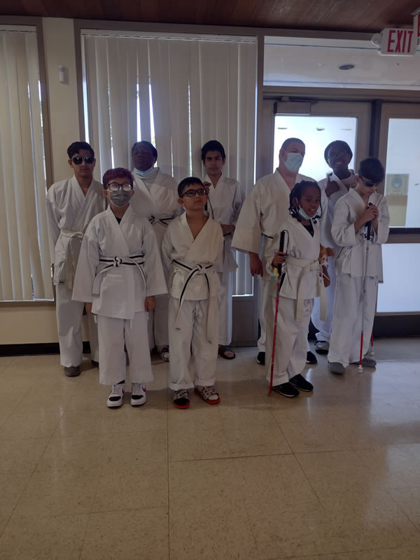 Nine students are standing in a school cafeteria wearing their Judo outfits.