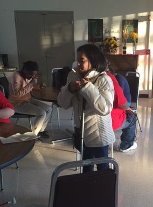 Student standing next to a table, holding a cane clutched in front of her.