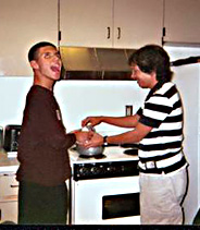 Two students cooking rice in a pot on a stove.